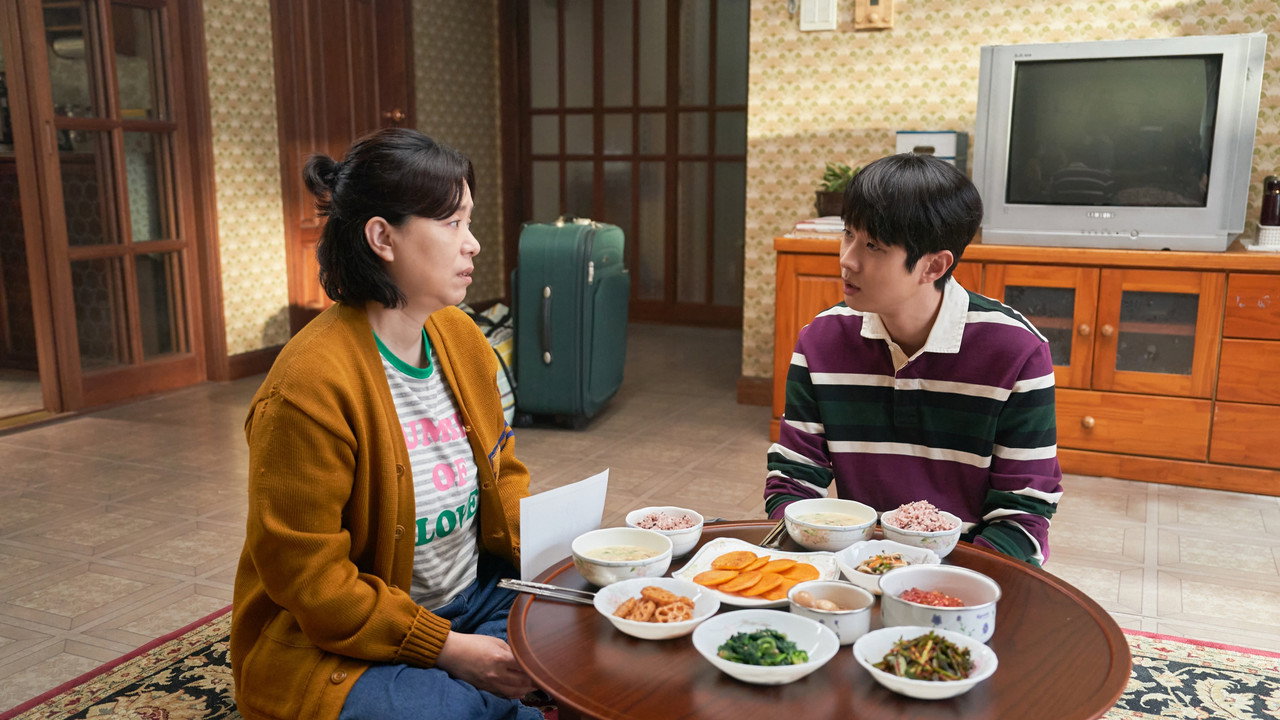 넘버원 거실 스틸. 최우식과 장혜진이 밥상 앞에 있고 뒤에 여행 가방과 브라운관 텔레비전이 있다