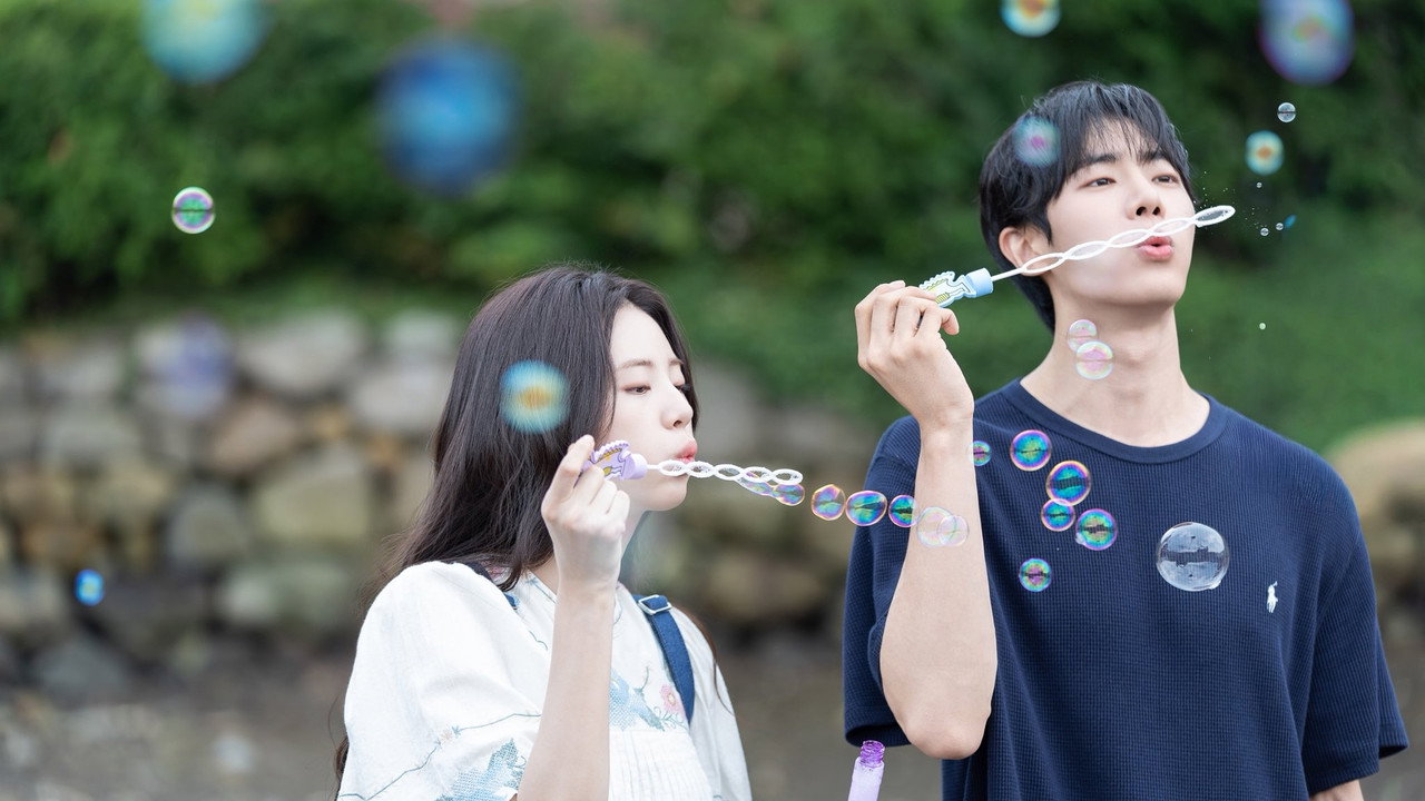 돌담 앞에서 신시아와 추영우가 비눗방울 막대를 부는 낮 스틸