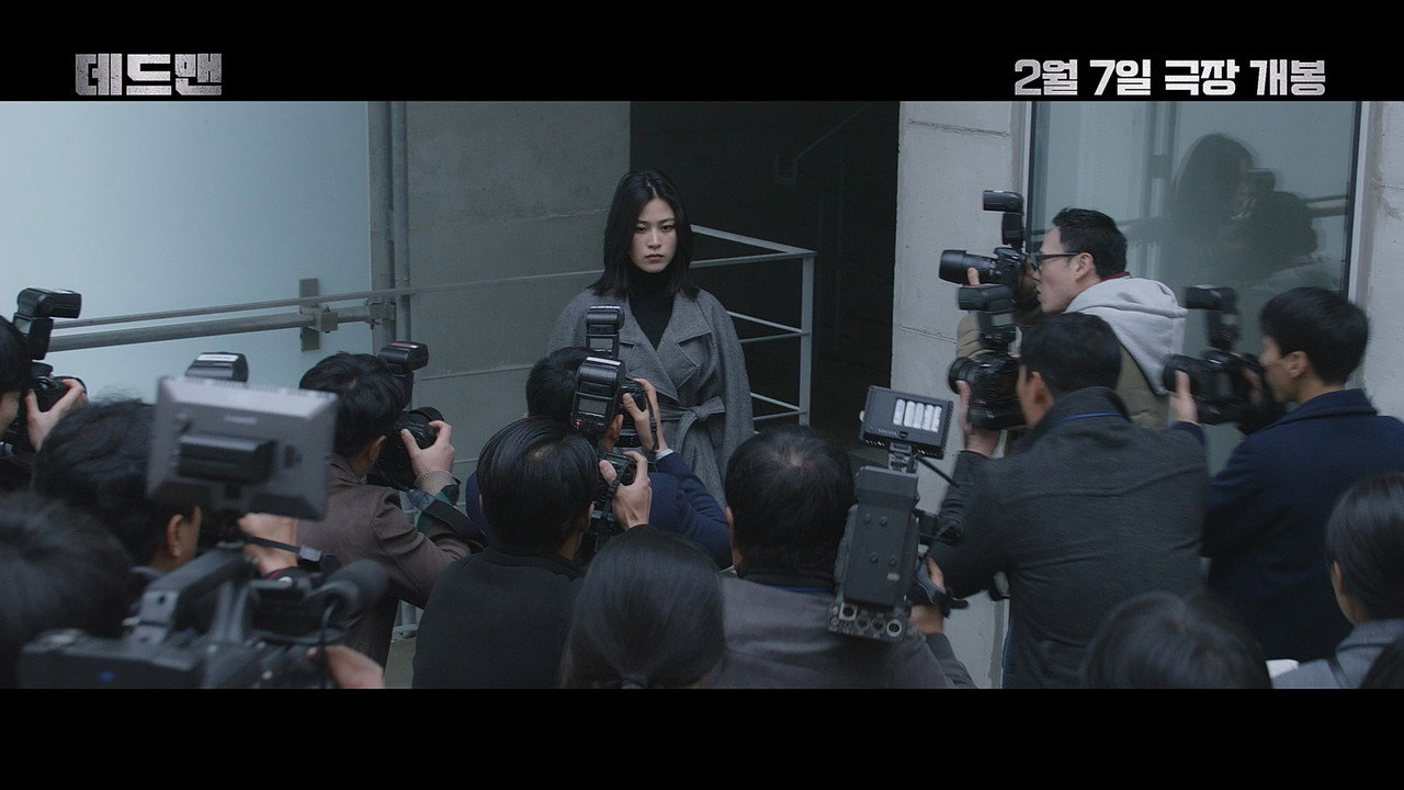 데드맨 스틸, 회색 코트의 여성이 취재 카메라에 둘러싸여 서 있다